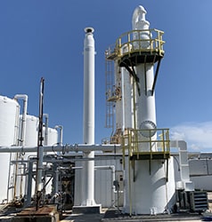 A caustic scrubber system consisting of a vertical packed media bed and pipes, used for treating noxious gas emissions in industrial processes.
